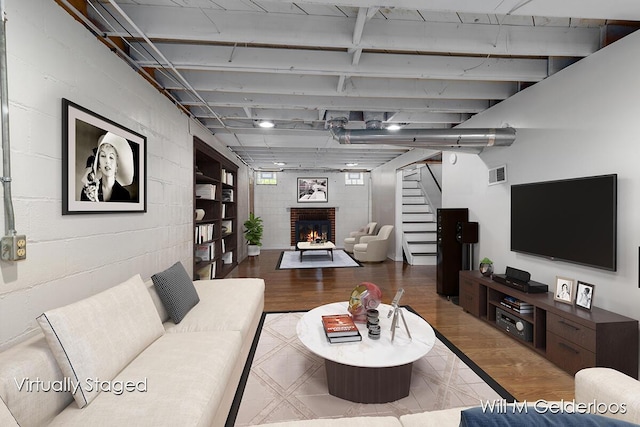 living area with wood finished floors, a brick fireplace, and stairway