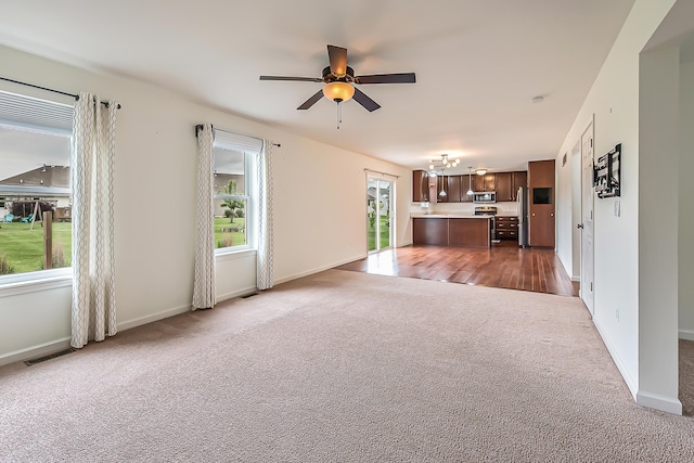 6837 Wellington Dr, Dexter, MI 48130 - unfurnished living room with dark carpet, ceiling fan, baseboards, and a chandelier