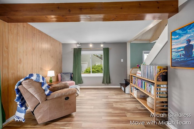 living area featuring wood finished floors, wooden walls, and beam ceiling