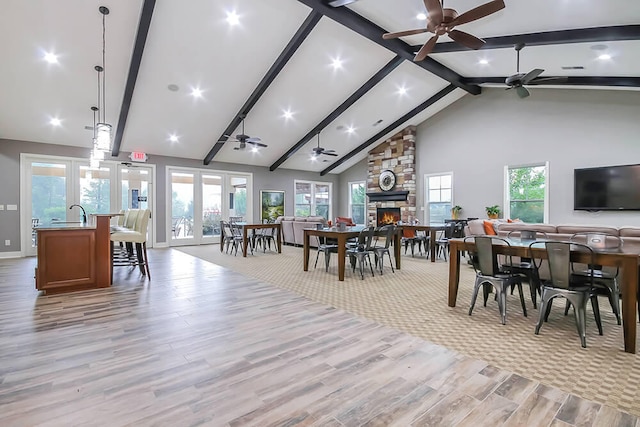 dining space featuring ceiling fan, beamed ceiling, high vaulted ceiling, light wood-style flooring, and a fireplace