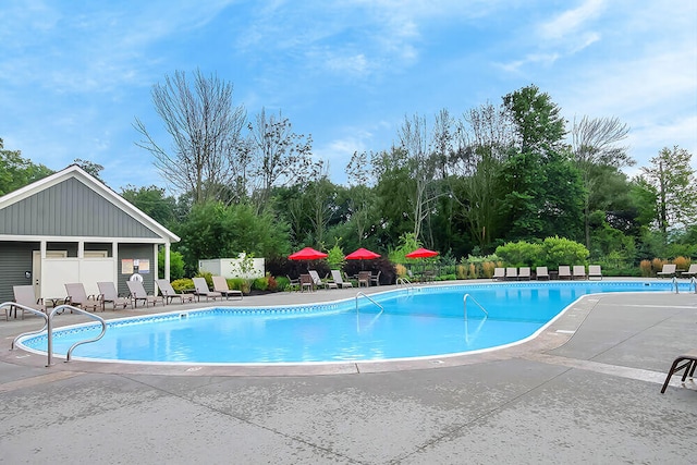 community pool featuring a patio, fence, and view of wooded area