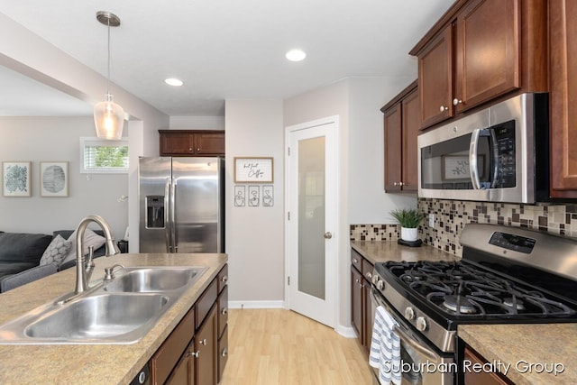 kitchen with stainless steel appliances, a sink, light wood-type flooring, decorative light fixtures, and backsplash