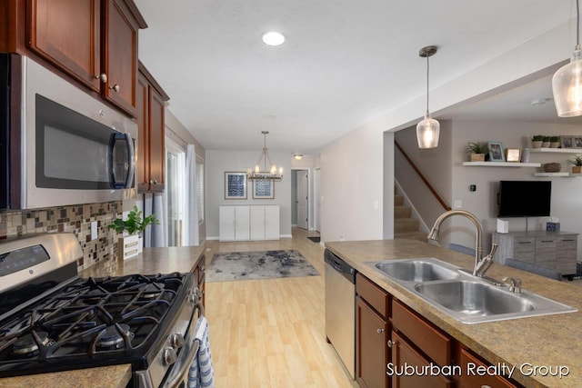 kitchen with appliances with stainless steel finishes, a sink, open floor plan, decorative light fixtures, and light wood-style flooring