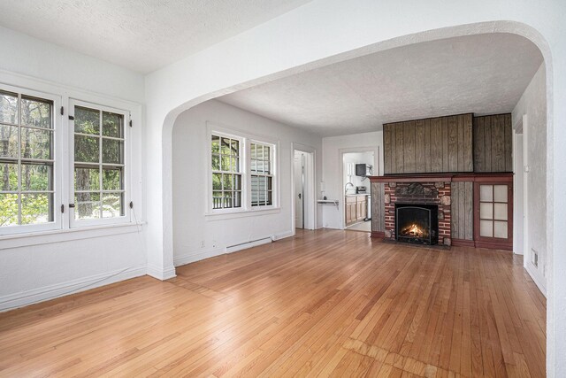 7566 Red Arrow Hwy, Stevensville, MI 49127 - unfurnished living room featuring light wood-type flooring, a baseboard heating unit, arched walkways, a brick fireplace, and a textured ceiling