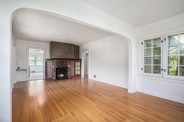 7566 Red Arrow Hwy, Stevensville, MI 49127 - unfurnished living room with light wood-style floors, arched walkways, ceiling fan, a fireplace, and baseboards