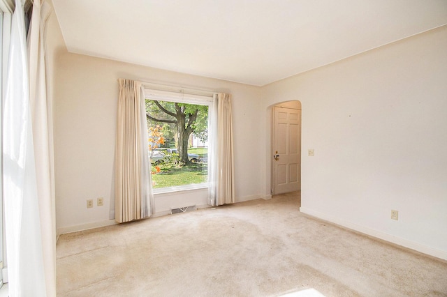 carpeted empty room featuring arched walkways and baseboards