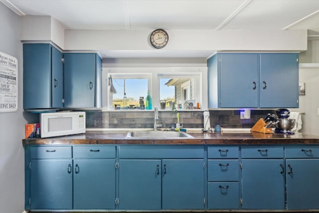 kitchen featuring white microwave, a sink, blue cabinetry, and dark countertops