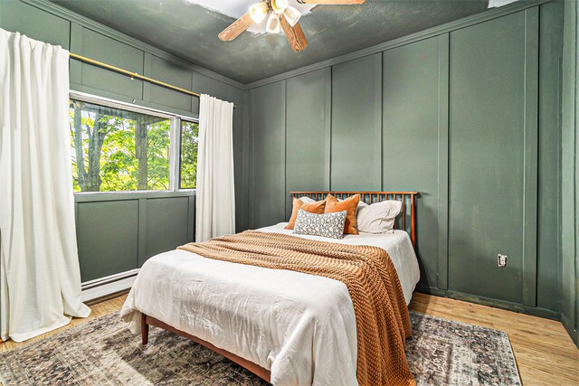 524 S Mears Ave, Whitehall, MI 49461 - bedroom featuring a decorative wall, wood finished floors, a baseboard heating unit, crown molding, and a ceiling fan