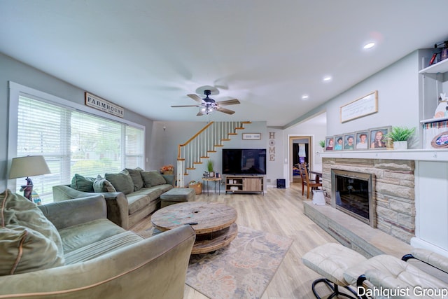 living area featuring a stone fireplace, ceiling fan, stairs, light wood-style floors, and recessed lighting