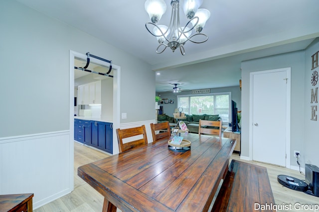 dining space with light wood finished floors, a chandelier, wainscoting, and ceiling fan