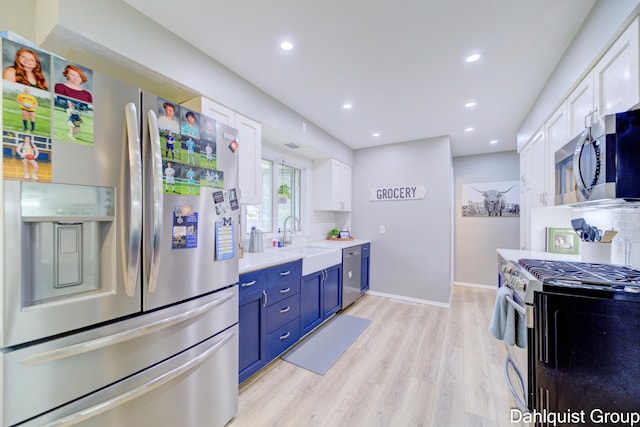 kitchen featuring stainless steel appliances, blue cabinetry, backsplash, white cabinets, and light wood-style floors