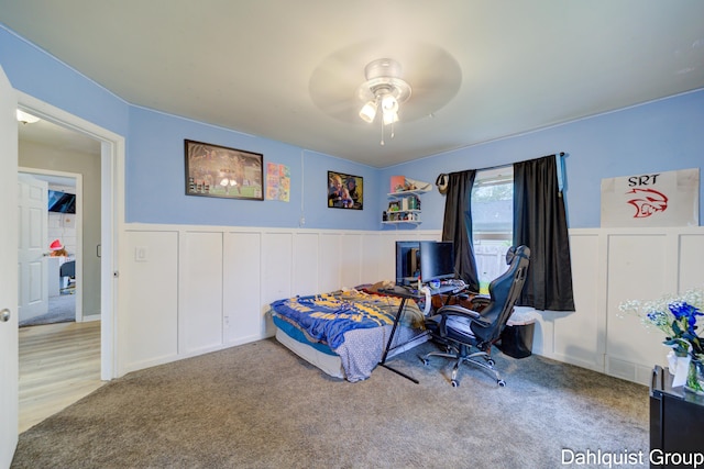 carpeted bedroom featuring a decorative wall, wainscoting, and a ceiling fan