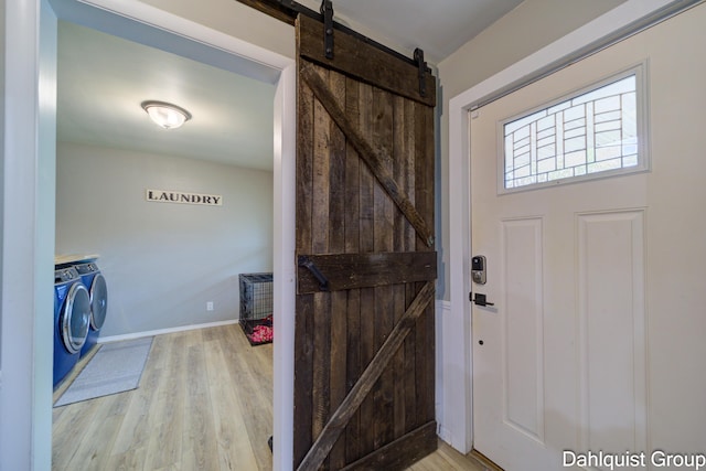 laundry area with washer and dryer, a barn door, light wood-type flooring, and baseboards