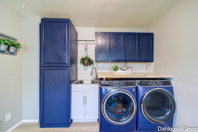 clothes washing area with cabinet space, washing machine and clothes dryer, light wood finished floors, and baseboards