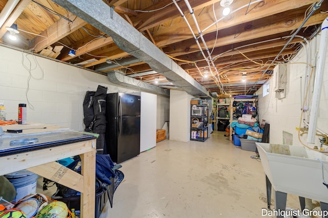 unfinished basement with freestanding refrigerator, a sink, and concrete block wall