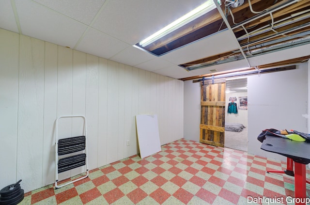finished below grade area featuring tile patterned floors, wood walls, heating unit, and a paneled ceiling