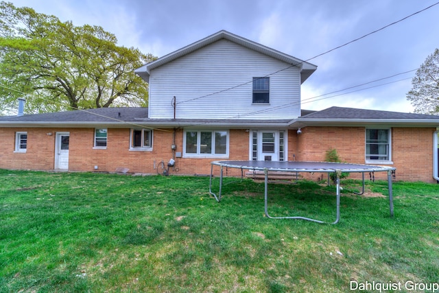 rear view of property featuring a trampoline, brick siding, and a yard