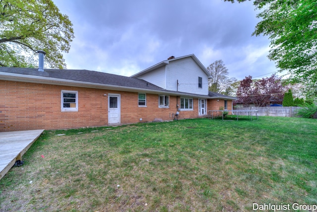 rear view of house with brick siding, a trampoline, and a wooden deck