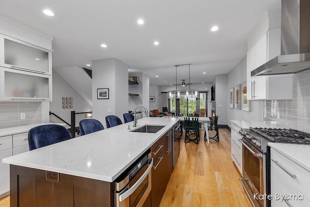 657 Greenslate Dr SE, Ada, MI 49301 - kitchen with appliances with stainless steel finishes, wall chimney range hood, light wood finished floors, a sink, and a large island with sink
