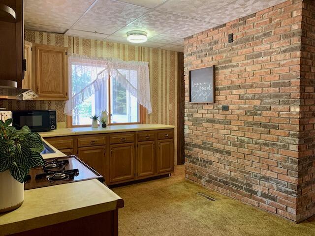 4827 W Unora Park Dr, Baldwin, MI 49304 - kitchen featuring wallpapered walls, black microwave, light carpet, light countertops, and range with gas cooktop