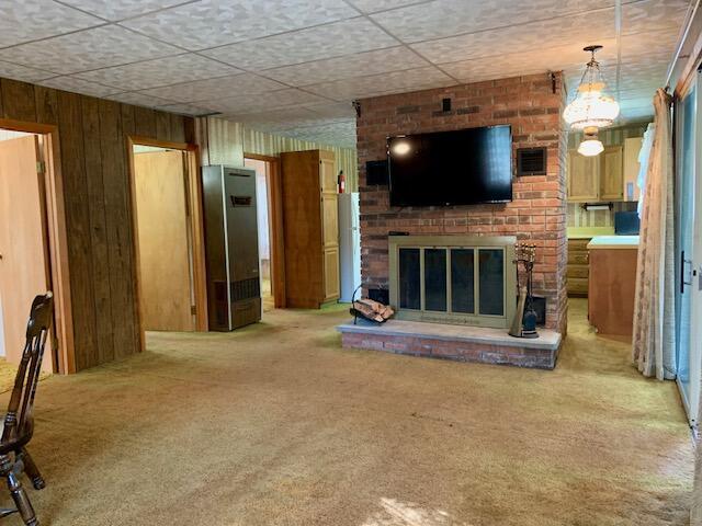 4827 W Unora Park Dr, Baldwin, MI 49304 - unfurnished living room featuring light carpet, a brick fireplace, wood walls, and a paneled ceiling