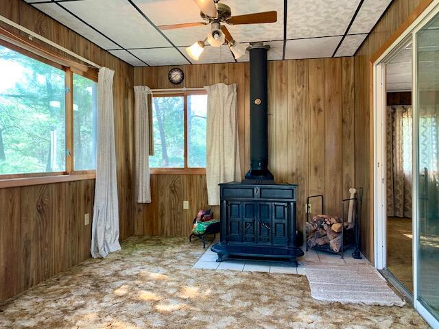 4827 W Unora Park Dr, Baldwin, MI 49304 - unfurnished living room featuring a wood stove, wooden walls, a ceiling fan, and carpet