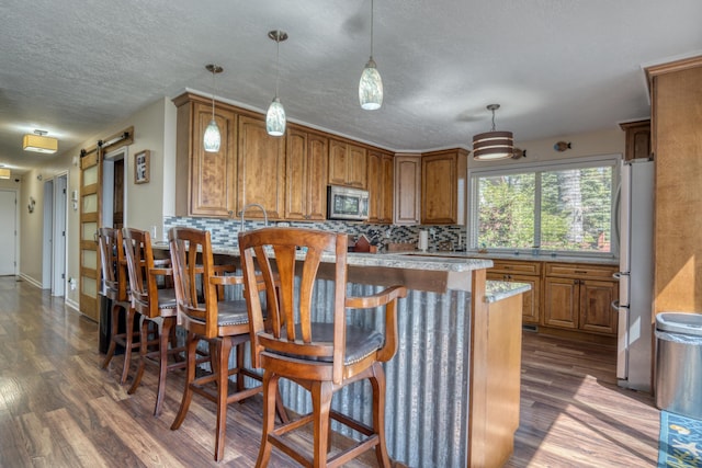 108 Eastbrook Ave, Houghton Lake, MI 48629 - kitchen with stainless steel appliances, a barn door, dark wood finished floors, brown cabinets, and a textured ceiling