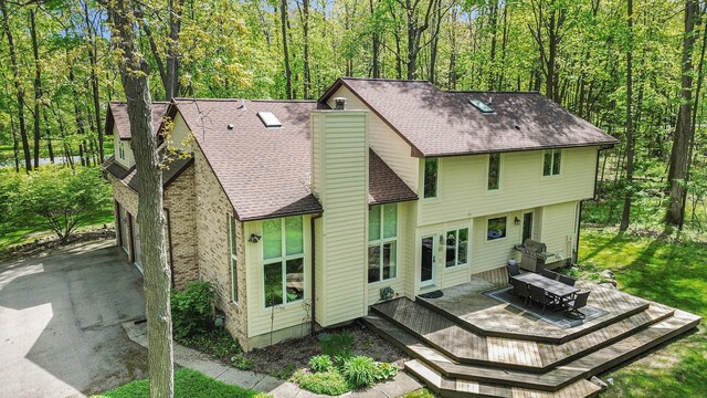 8461 Webster Hills Rd, Dexter, MI 48130 - rear view of house with a chimney, a deck, roof with shingles, and a view of trees