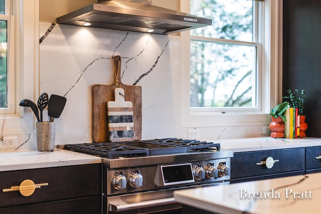 2100 Timber Point Dr SE, Ada, MI 49301 - kitchen with stainless steel range with gas stovetop, wall chimney exhaust hood, light stone counters, and tasteful backsplash