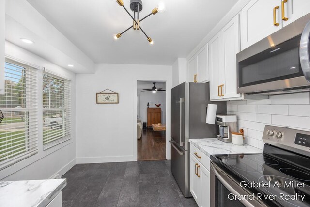 kitchen with appliances with stainless steel finishes, white cabinetry, backsplash, a chandelier, and light stone countertops