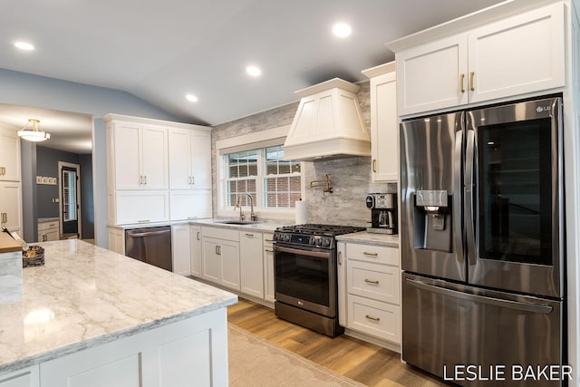 833 Allen Dr, Holland, MI 49423 - kitchen featuring appliances with stainless steel finishes, premium range hood, a sink, light wood-style floors, and vaulted ceiling