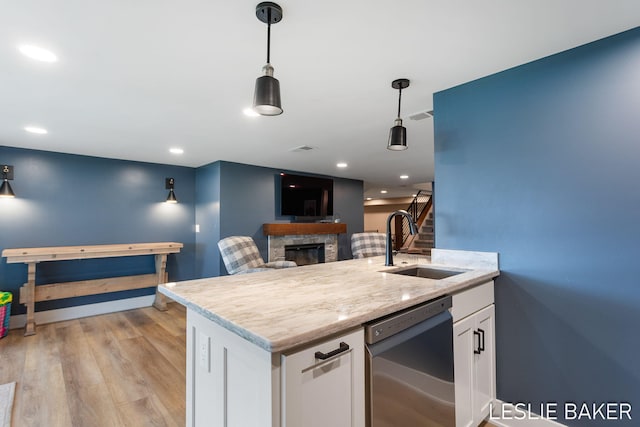 833 Allen Dr, Holland, MI 49423 - kitchen featuring stainless steel dishwasher, a sink, a fireplace, white cabinets, and decorative light fixtures