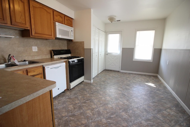 kitchen featuring white appliances, a sink, brown cabinets, wainscoting, and stone finish flooring