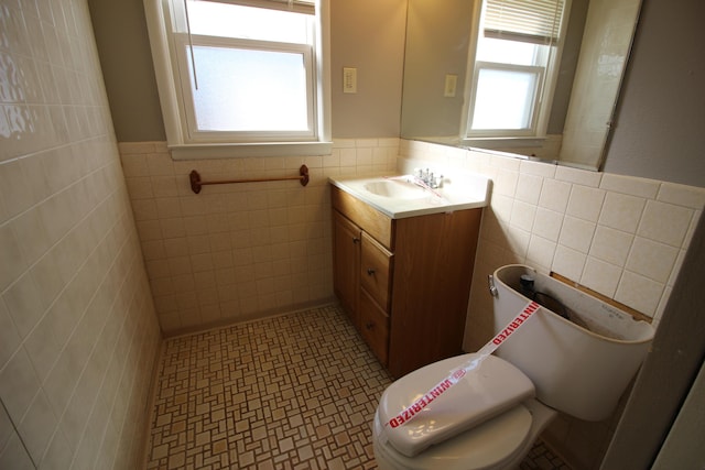 bathroom with tile walls, healthy amount of natural light, wainscoting, vanity, and toilet