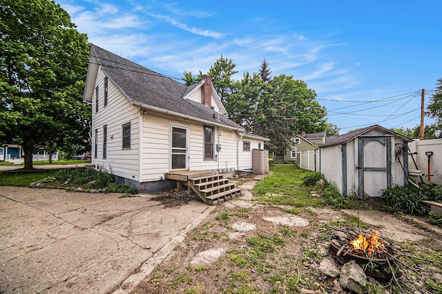 237 E Main St, Milan, MI 48160 - rear view of house featuring an outdoor fire pit, a storage unit, an outbuilding, roof with shingles, and a chimney