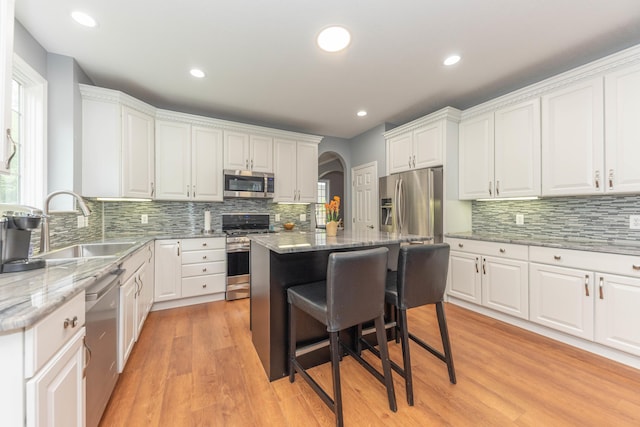 1218 Waterways Dr, Ann Arbor, MI 48108 - kitchen with appliances with stainless steel finishes, a sink, arched walkways, white cabinets, and tasteful backsplash