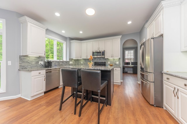 1218 Waterways Dr, Ann Arbor, MI 48108 - kitchen with appliances with stainless steel finishes, white cabinets, tasteful backsplash, a kitchen island, and arched walkways