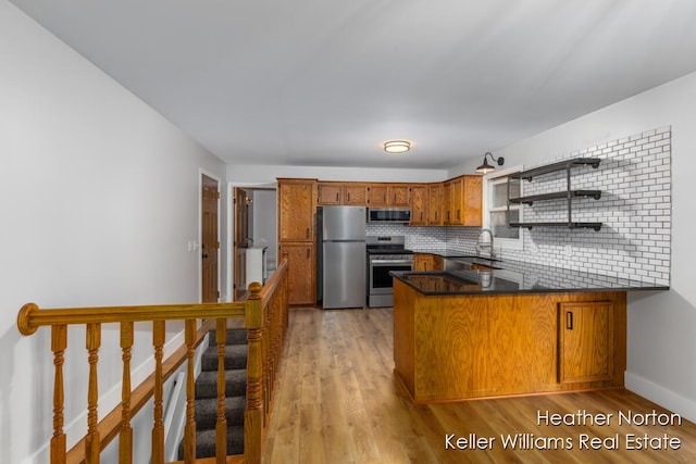 kitchen with stainless steel appliances, a peninsula, brown cabinets, and light wood-type flooring