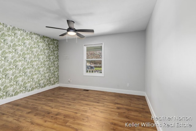 spare room featuring wallpapered walls, baseboards, a ceiling fan, wood finished floors, and an accent wall