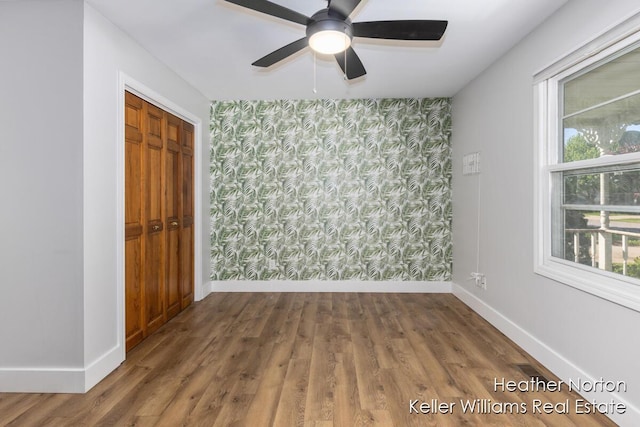 unfurnished room with wallpapered walls, an accent wall, baseboards, wood finished floors, and a ceiling fan