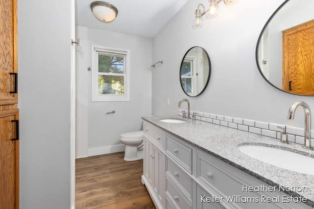 bathroom featuring wood finished floors, baseboards, toilet, and double vanity