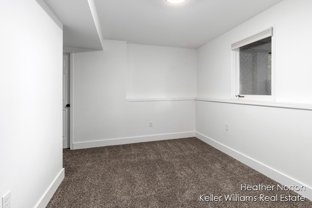 spare room featuring dark carpet and baseboards