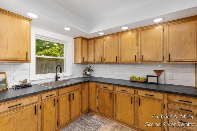 kitchen with a sink, recessed lighting, brown cabinets, light wood-type flooring, and backsplash