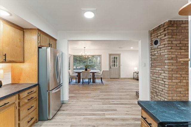 kitchen featuring freestanding refrigerator, dark countertops, brick wall, light wood-style flooring, and a chandelier