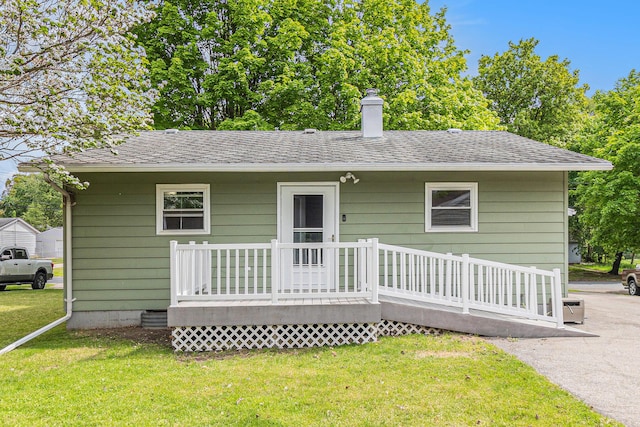 rear view of property with a deck, a lawn, a chimney, and a shingled roof