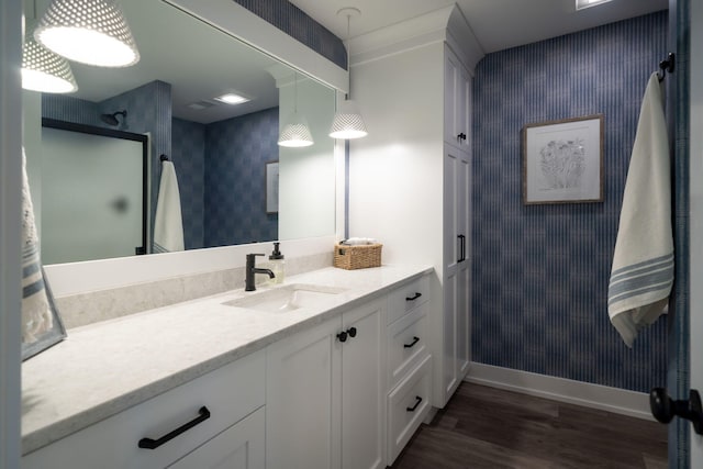 bathroom featuring wood finished floors, baseboards, wallpapered walls, vanity, and a shower