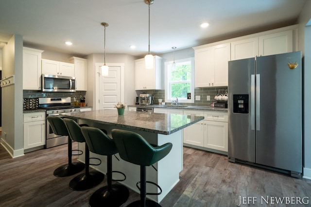 kitchen with stainless steel appliances, a sink, dark wood-style flooring, decorative backsplash, and white cabinets