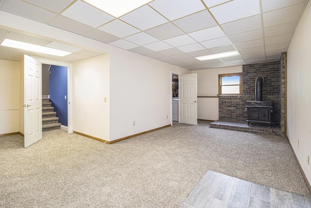6001 Dover Ln, Traverse City, MI 49684 - unfurnished living room featuring a wood stove, a drop ceiling, carpet, baseboards, and stairway