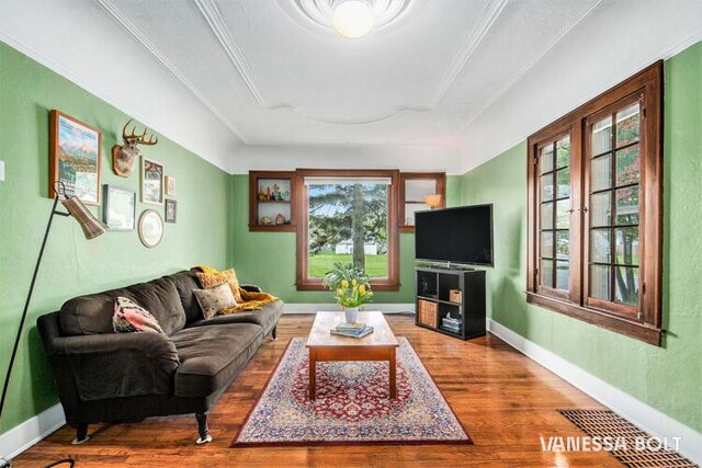living area with wood finished floors, crown molding, a tray ceiling, and baseboards
