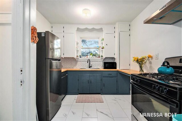 kitchen featuring black appliances, under cabinet range hood, a sink, light marble finish flooring, and backsplash